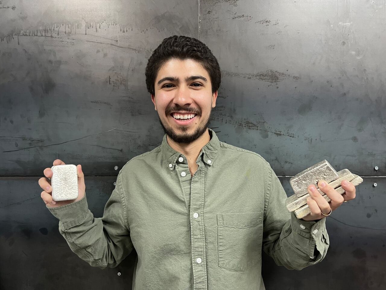 A man holds up silver bars.