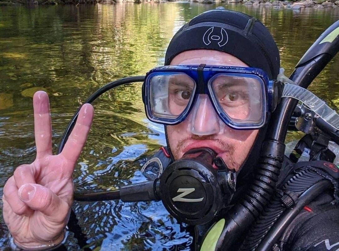 A man holds up a peace sign while taking a selfie in a wet suit.