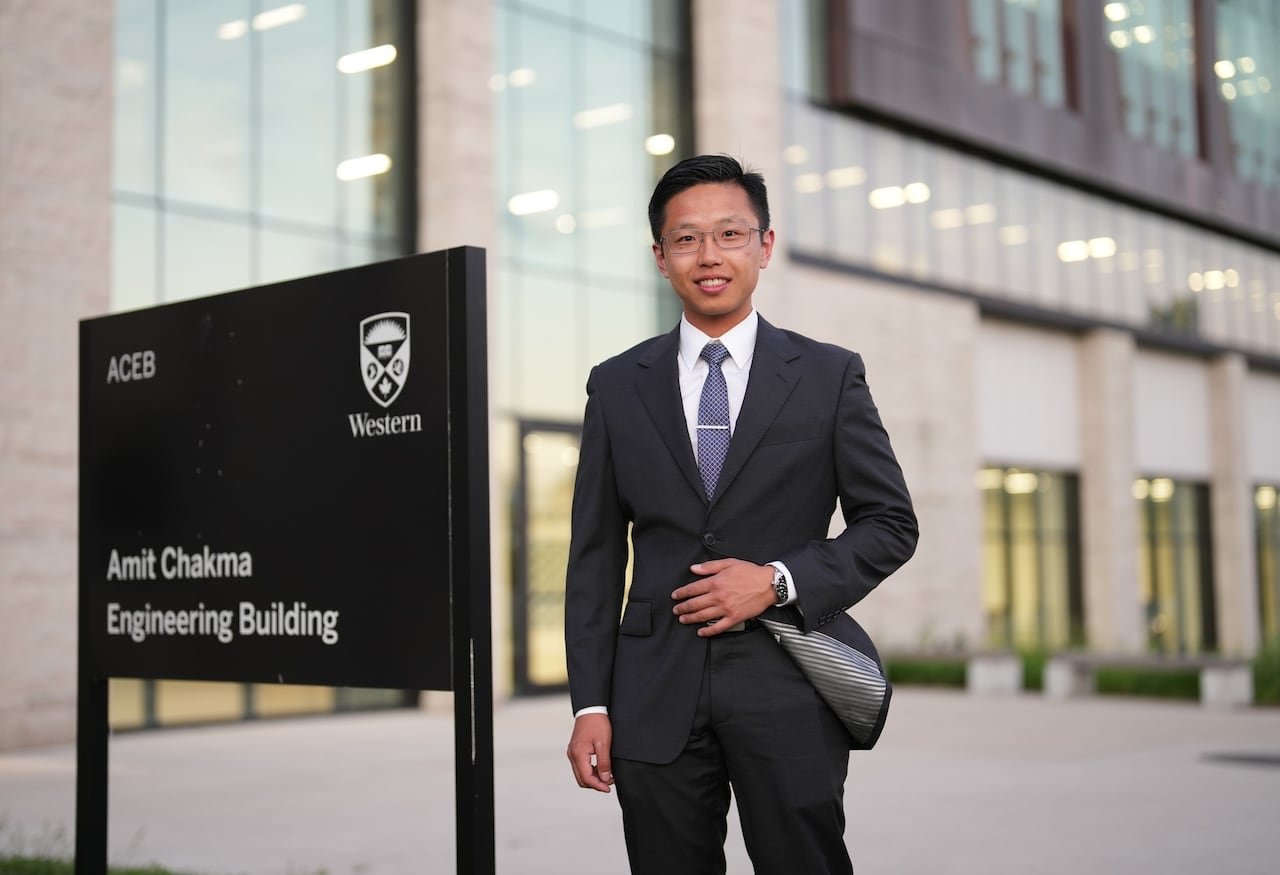 default-4737 A man in a suit smiles next to a sign for the Amit Chakma Engineering Building with a Western logo on it.