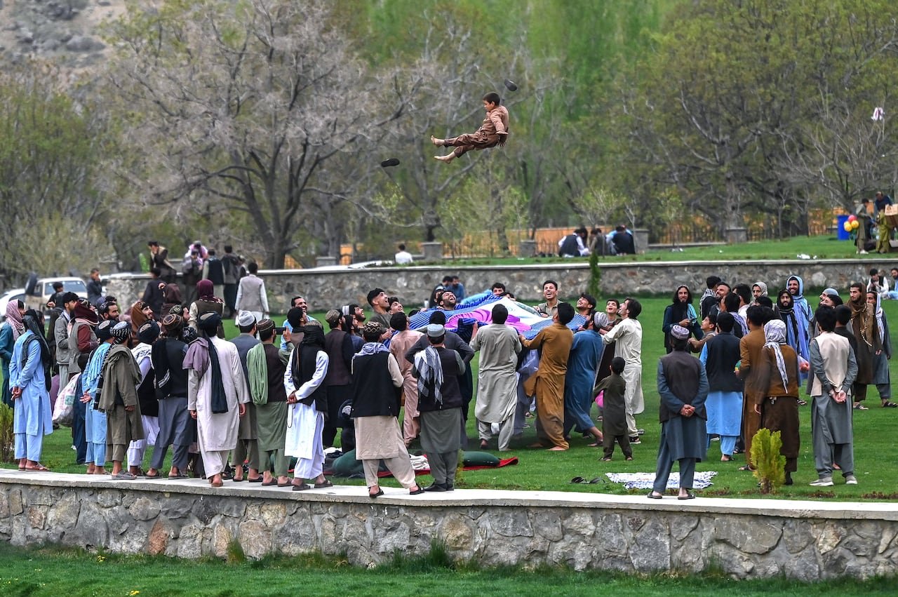 A wide shot of a group of men using a blanket to catapult a boy in the air, and catch him when he comes down.